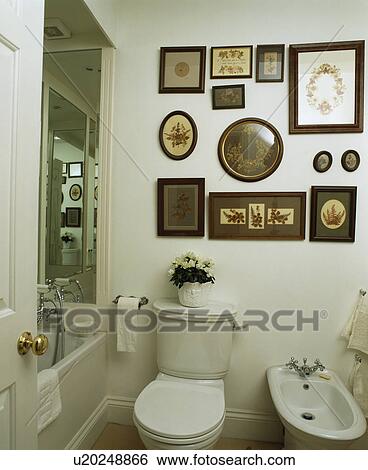 Stock Photograph - Collection of pictures above toilet and bidet in small white bathroom. Fotosearch