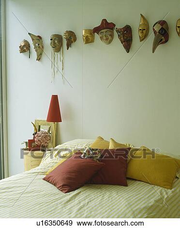 Stock Photo - Collection of small ceramic masks above bed with red and yellow cushions. Fotosearch