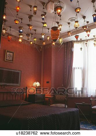 Stock Image - Colourful lighted glass lanterns suspended from ceiling in red bedroom in Turkish hotel. Fotosearch