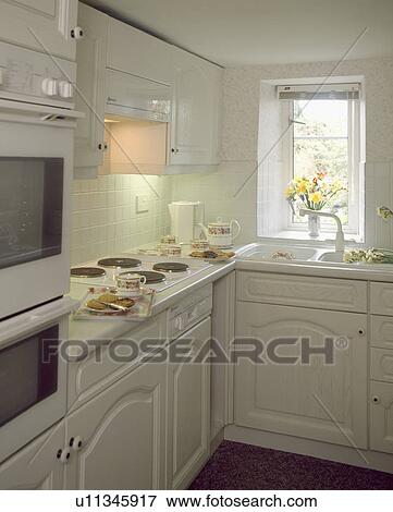 Stock Photo - Compact white cottage kitchen with fitted units and electric hob. Fotosearch