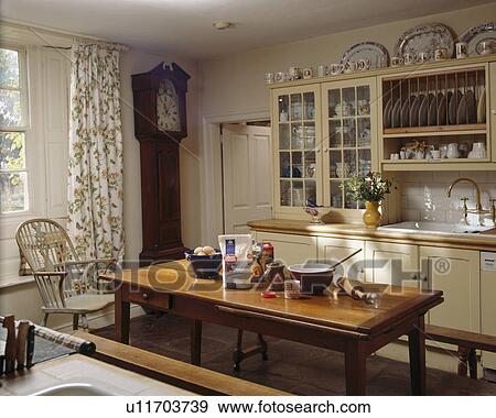 Cookery ingredients and bowls on wooden table in small cream kitchen with longcase clock View Large Photo Image Stock Photo - Cookery ingredients and bowls on wooden table in small cream kitchen with longcase clock. Fotosearch
