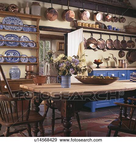 Stock Photo - Copper pans and blue china on shelves in cottage dining room with wooden table. Fotosearch