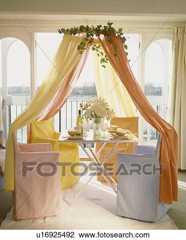 Coronet with orange and yellow voile drapes above table and director's chairs with blue, pink and yellow pastel loosecovers View Large Photo Image Stock Image - Coronet with orange and yellow voile drapes above table and director's chairs with blue, pink and yellow pastel loosecovers. Fotosearch