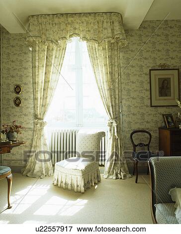 Stock Photo - Country bedroom with small upholstered chair in front of window with blue+cream patterned curtains and pelmet. Fotosearch