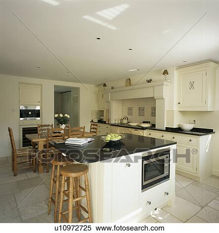Country kitchen with wooden stools at breakfast bar on granite-topped island unit with fitted microwave oven View Large Photo Image Stock Photography - Country kitchen with wooden stools at breakfast bar on granite-topped island unit with fitted microwave oven . Fotosearch