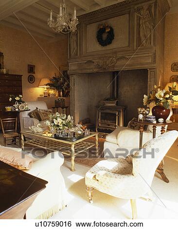 Cream armchair and sofas in French country living room with wood-burning stove in large ornate stone fireplace View Large Photo Image Stock Photograph - Cream armchair and sofas in French country living room with wood-burning stove in large ornate stone fireplace. Fotosearch