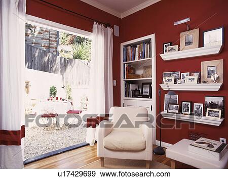 Cream armchair beside open doorway with view of patio in red living room with photographs on shelves View Large Photo Image Stock Photo - Cream armchair beside open doorway with view of patio in red living room with photographs on shelves. Fotosearch