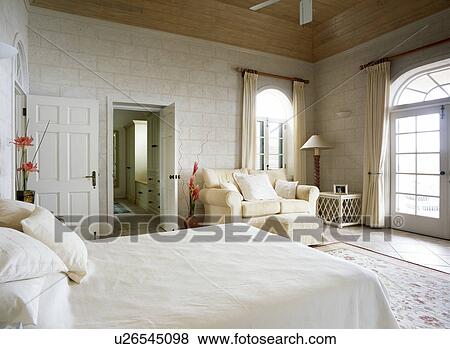 Cream bedlinen and sofa in bedroom with white walls View Large Photo Image Stock Photo - Cream bedlinen and sofa in bedroom with white walls. Fotosearch