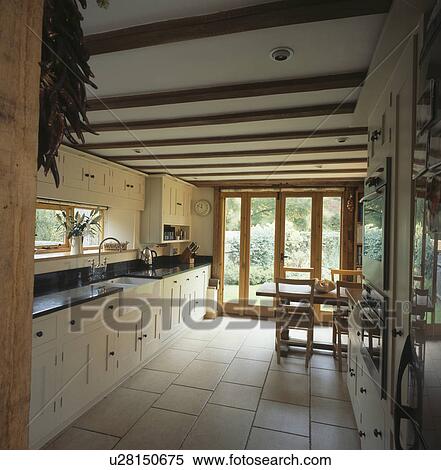 Stock Photography - Cream ceramic floor tiles in country kitchen with cream fitted units. Fotosearch