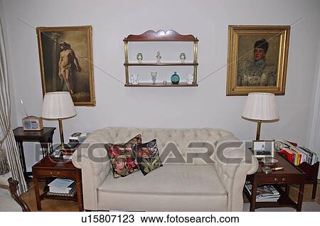 Cream lamps on tables on either side of beige Chesterfield sofa in apartment living room View Large Photo Image Stock Image - Cream lamps on tables on either side of beige Chesterfield sofa in apartment living room. Fotosearch