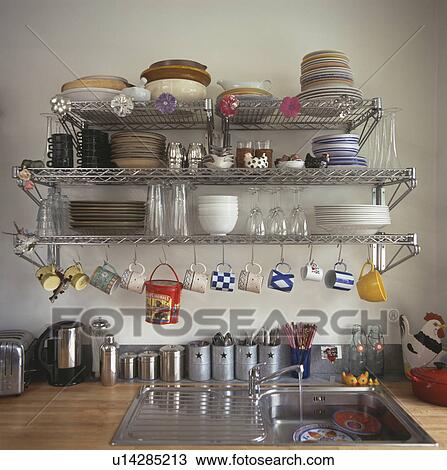 Stock Image - Crockery and pans on stainless steel storage shelves above kitchen sink. Fotosearch