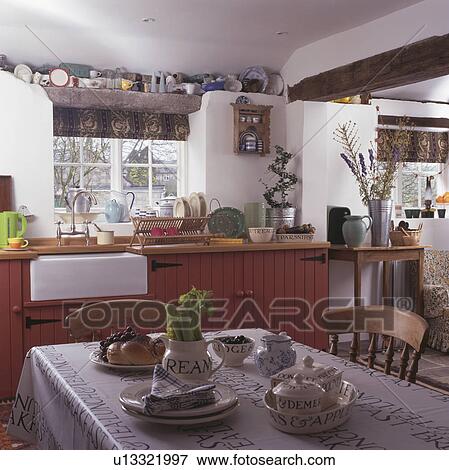 Crockery on table with black+white cloth in white cottage kitchen with pink units View Large Photo Image Stock Photo - Crockery on table with black+white cloth in white cottage kitchen with pink units. Fotosearch