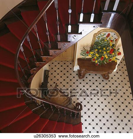 Stock Image - Curved staircase with red carpet in hall with black+white chequerboard floor. Fotosearch