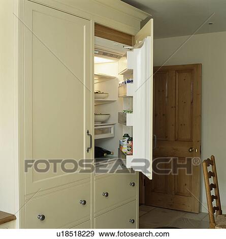 Stock Photo - Door open of fridge in fitted cream kitchen storage cupboard. Fotosearch