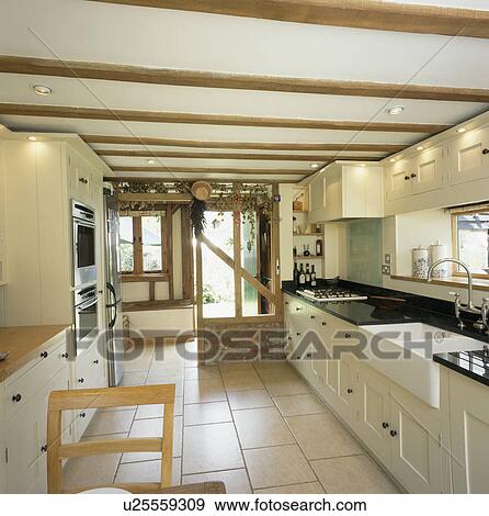 Stock Photo - Double Belfast sink in cream country kitchen with cream flooring and downlighting. Fotosearch