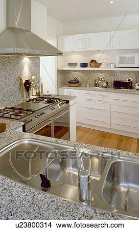 Double stainless steel sink and range oven in modern kitchen with fitted white units and grey granite worktops View Large Photo Image Picture - Double stainless steel sink and range oven in modern kitchen with fitted white units and grey granite worktops. Fotosearch