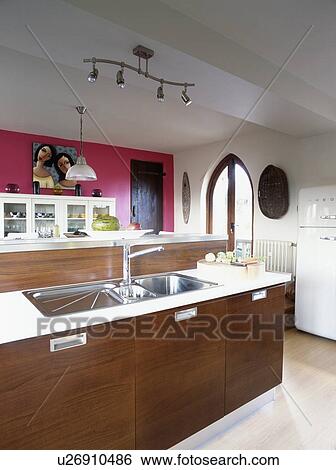 Double stainless steel sinks in brown island unit in modern white kitchen with red wall View Large Photo Image Stock Photograph - Double stainless steel sinks in brown island unit in modern white kitchen with red wall. Fotosearch