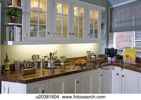 Picture - Downlighting in and below glass-fronted fitted wall cupboards in traditional kitchen with black walnut worktops. Fotosearch