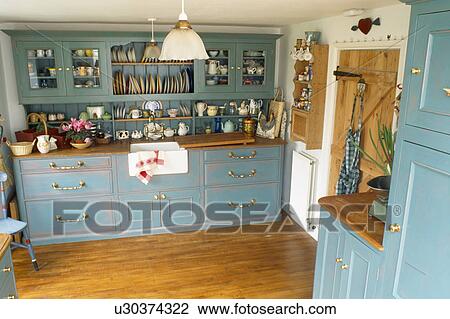 Stock Image - Fitted blue dresser in country kitchen with wooden flooring. Fotosearch