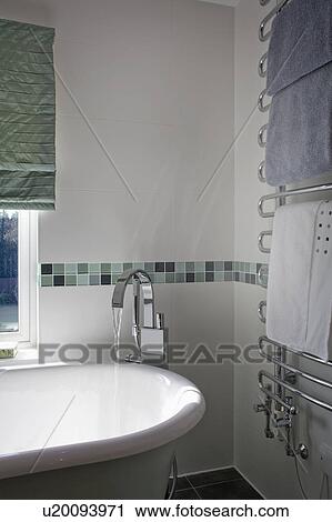 Stock Image - Floor-mounted bath-column mixer tap and roll-top bath in modern bathroom with heated towel rail. Fotosearch
