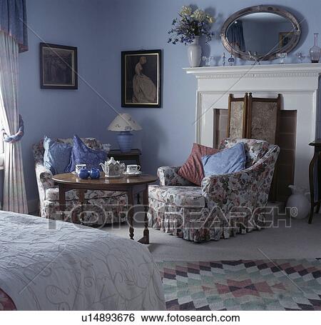 Floral armchair and circular table iin front of fireplace in blue country bedroom View Large Photo Image Stock Photograph - Floral armchair and circular table iin front of fireplace in blue country bedroom. Fotosearch