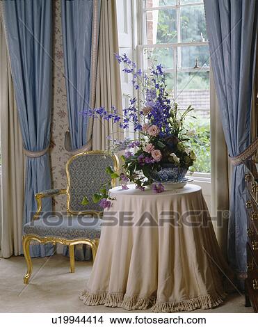 Floral arrangement on table with cream cloth in front of window with blue curtains View Large Photo Image Picture - Floral arrangement on table with cream cloth in front of window with blue curtains. Fotosearch