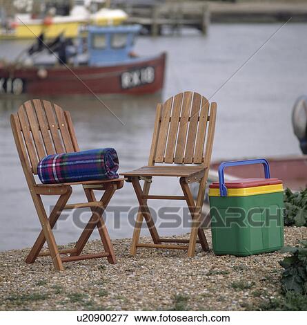Fold-up wooden chairs and brightly-coloured plastic cool-box on harbour wall View Large Photo Image Stock Photo - Fold-up wooden chairs and brightly-coloured plastic cool-box on harbour wall. Fotosearch