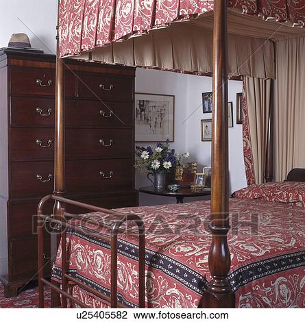 Stock Image - Four-poster bed with pink patterned drapes and bedlinen in cottage bedroom. Fotosearch