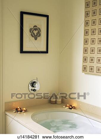 Stock Image - Framed seaside pebbles above lighted candles on bath. Fotosearch