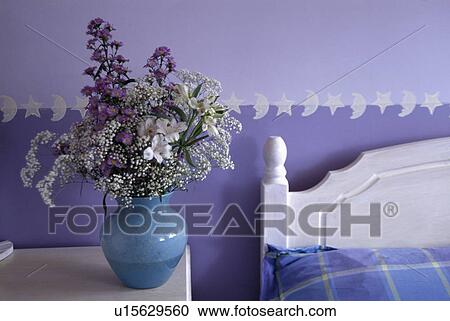 Stock Image - Fresh flowers in blue vase on bedside table in blue bedroom. Fotosearch
