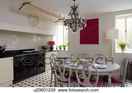 Georgian crystal chandelier above pale grey table and chairs in kitchen with black Aga oven and chequerboard flooring View Large Photo Image Stock Photo - Georgian crystal chandelier above pale grey table and chairs in kitchen with black Aga oven and chequerboard flooring. Fotosearch
