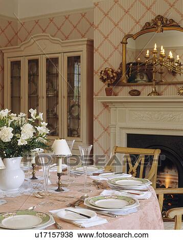 Stock Photo - Gilt mirror above candelabra on mantelpiece in dining room with pink trellis wallpaper and white crockery on pink cloth. Fotosearch