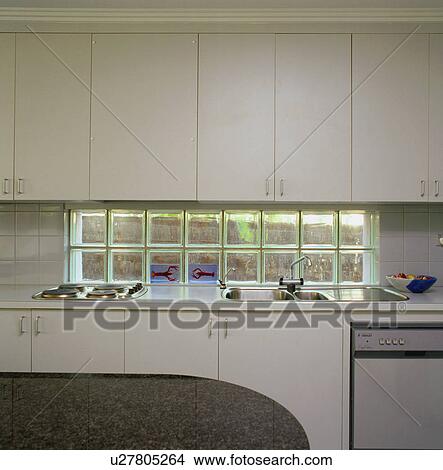 Glass brick window between fitted white cupboards and fitted hob and sink in modern white kitchen View Large Photo Image Picture - Glass brick window between fitted white cupboards and fitted hob and sink in modern white kitchen. Fotosearch