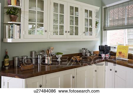 Stock Photograph - Glass-fronted fitted wall cupboards in traditional kitchen with black walnut worktops. Fotosearch