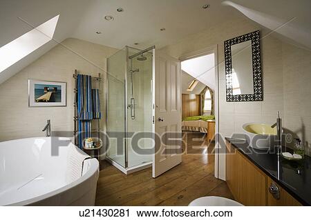 Glass shower cabinet and wood flooring in large ensuite attic bathroom with door open to bedroom View Large Photo Image Stock Image - Glass shower cabinet and wood flooring in large ensuite attic bathroom with door open to bedroom. Fotosearch
