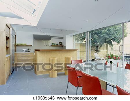 Glass-topped dining table and red leather chairs in modern open plan kitchen dining room with stone floor tiles and oak units View Large Photo Image Stock Image - Glass-topped dining table and red leather chairs in modern open plan kitchen dining room with stone floor tiles and oak units. Fotosearch