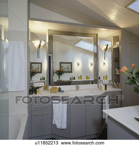 Stock Image - Glass wall-lights on either side of mirror above basin in modern grey bathroom. Fotosearch