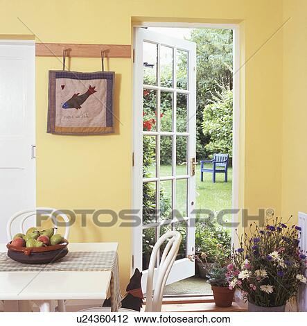 Stock Image - Glazed door open to garden in traditional yellow kitchen. Fotosearch