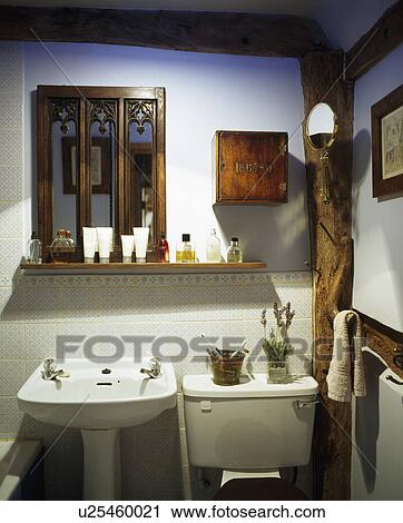 Stock Image - Gothic-style mirror and small wooden cupboard on wall above basin. Fotosearch