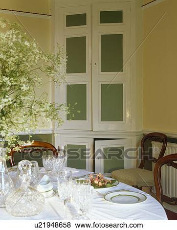 Stock Photo - Green painted fitted cupboard in country dining room with place settings on table. Fotosearch