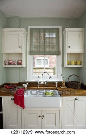 Green Pinoleum blind on window above white ceramic double sink in kitchen with cream fitted cupboards  View Large Photo Image Stock Photo - Green Pinoleum blind on window above white ceramic double sink in kitchen with cream fitted cupboards . Fotosearch
