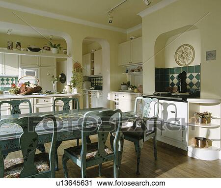 Stock Image - Hand-painted floral decoration on pale blue chairs and table in traditional kitchen with wooden flooring and white Aga. Fotosearch