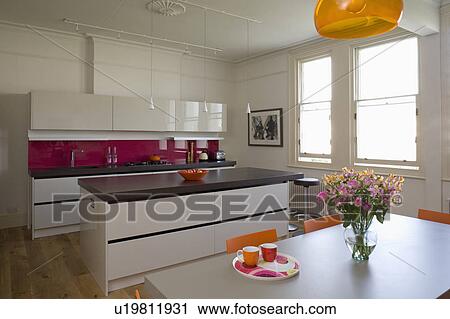 Stock Image - Island unit with cast concrete resin worktop in modern kitchen with white gloss lacquer units. Fotosearch