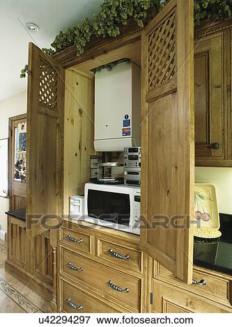 Stock Photo - Kitchen cupboard with central heating boiler above microwave oven and small hi-fi unit. Fotosearch