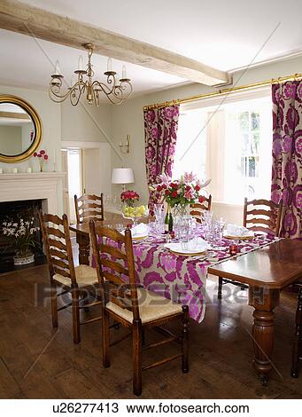 Stock Image - Ladderback chairs at table set for lunch in country dining room with pink cut-velvet Designer's Guild curtains and cloth. Fotosearch