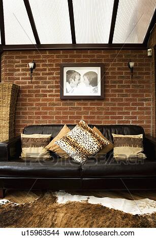 Picture - Large photograph on brick wall above black leather sofa with animalprint cushions in newbuild conservatory living room. Fotosearch