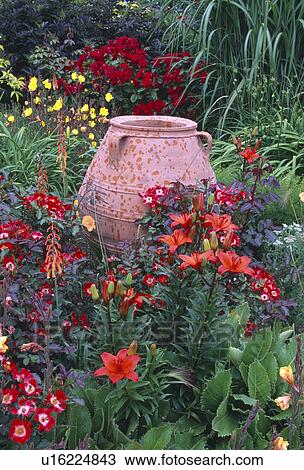 Stock Image - Large pithoi pot in summer garden border with red lilies and red Rosa Eyepaint. Fotosearch