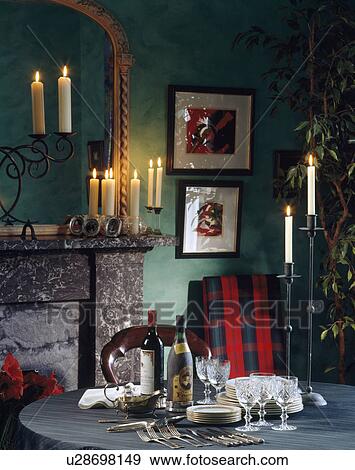 Stock Photo - Lighted candles on mantelpiece and table with wine and glasses in green dining room with red tartan throw on chair. Fotosearch