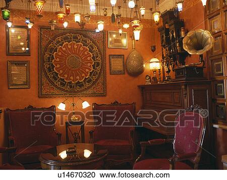Stock Image - Lighted glass lanterns hanging from ceiling in red hotel lounge in Turkey with group of pictures on walls . Fotosearch
