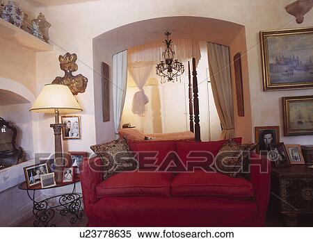 Lighted lamp on table beside red sofa in Majorcan cottage livingroom with archway to bedroom View Large Photo Image Stock Photography - Lighted lamp on table beside red sofa in Majorcan cottage livingroom with archway to bedroom. Fotosearch